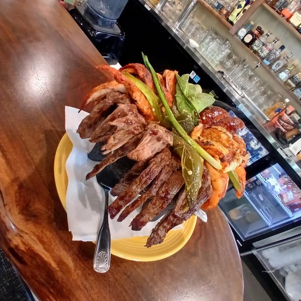 A large Mexican molcajete dish filled with grilled meats, peppers, and vegetables on a bar.