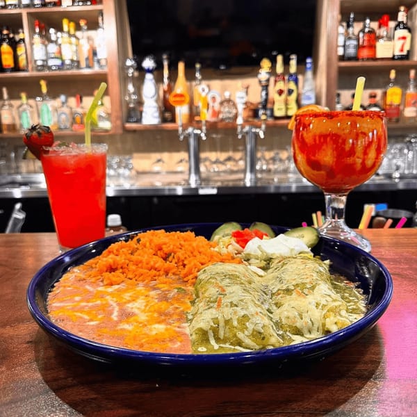 A plate of enchiladas, rice, and beans with two cocktails on a bar counter at Las Palmas Mexican Cuisine.