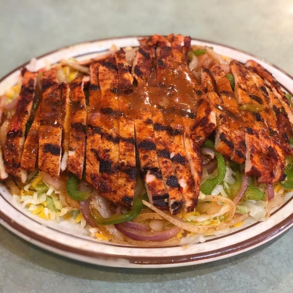 Grilled chicken strips with sauce, bell peppers, and onions on a bed of lettuce and cheese.