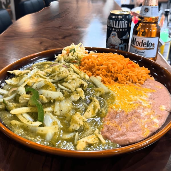 A plate of Mexican food with green chili chicken, rice, refried beans, and coleslaw, with two beers.